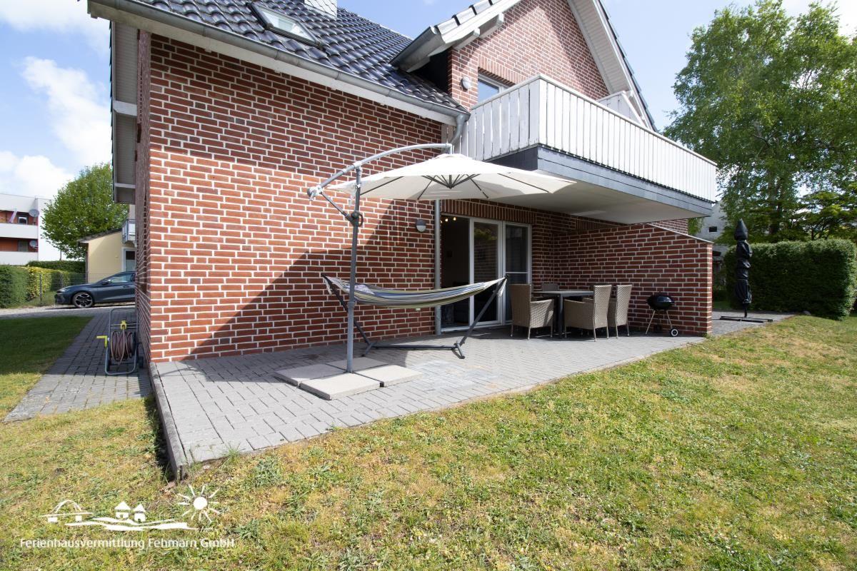 Haus mit Terrasse, Hängematte, Tisch und Stühlen sowie Grill und Sonnenschirm.