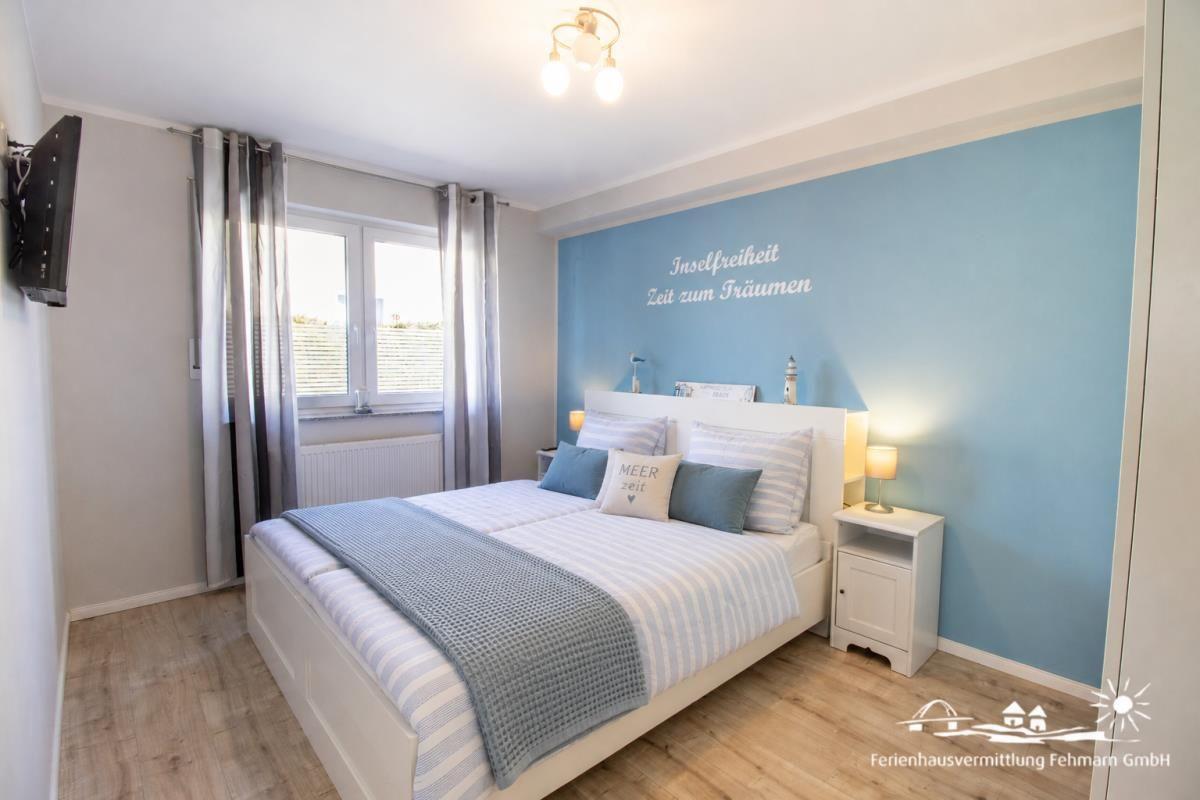 Schlafzimmer mit Bett, Nachttisch und Fenster. Wand mit Schriftzug.
