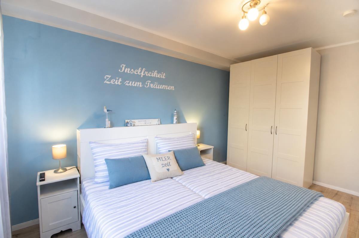 Schlafzimmer mit Bett, Nachttisch und Kleiderschrank. Wand mit Schriftzug.