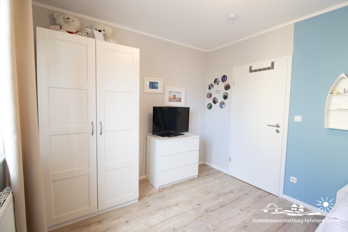 Schlafzimmer mit weißem Schrank, Fernseher und blauer Wand.