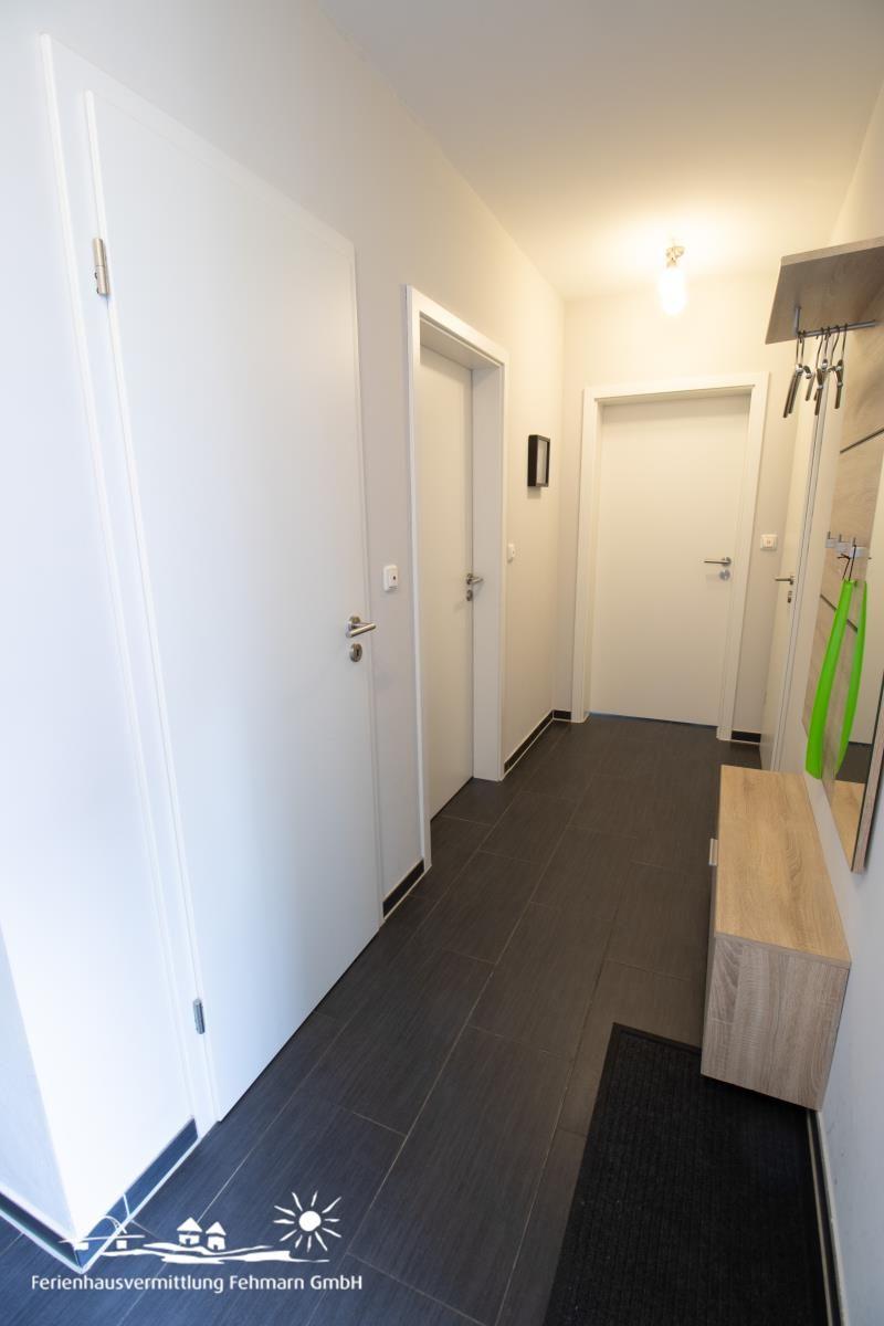 Flur mit dunklem Boden, weißen Türen und Holzbank mit Haken.