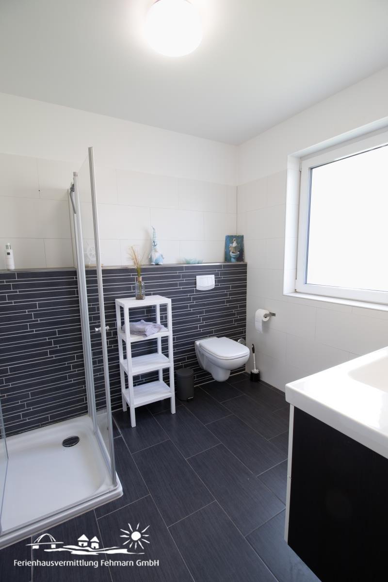 Badezimmer mit Dusche, Toilette und Waschtisch. Wandfliesen und Bodenfliesen in Schwarz-Weiß.