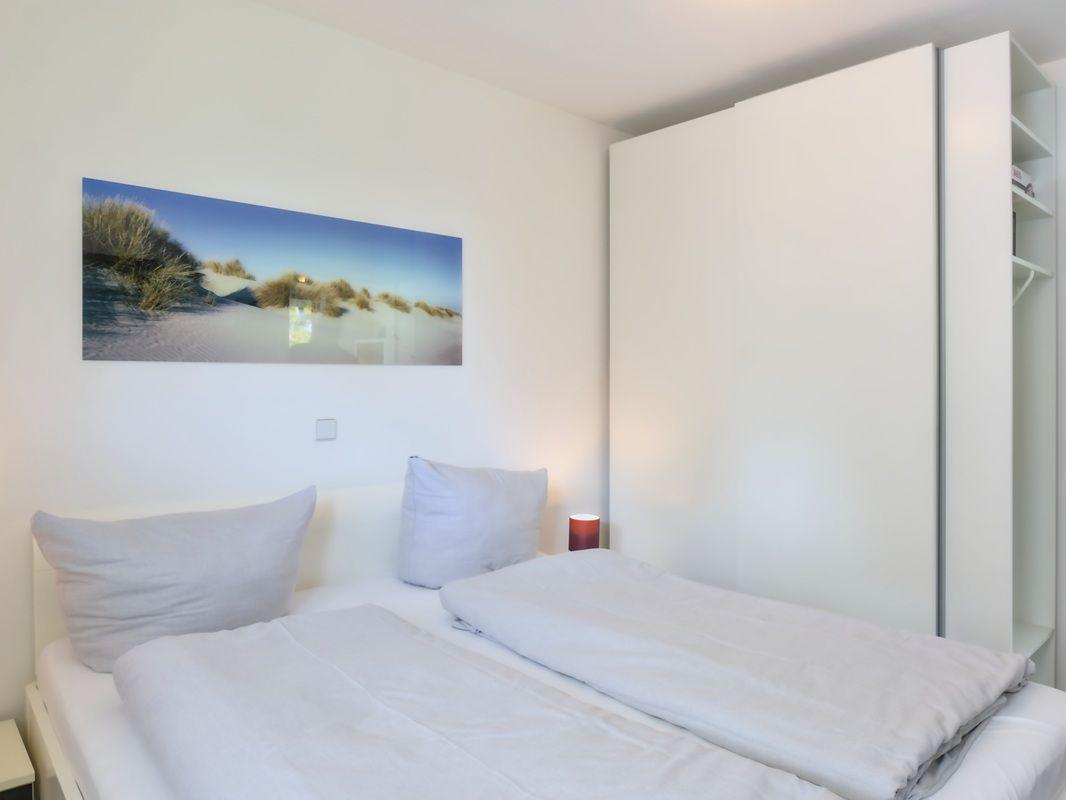 Schlafzimmer mit Doppelbett, weißen Kissen und Wandbild mit Strandmotiv.