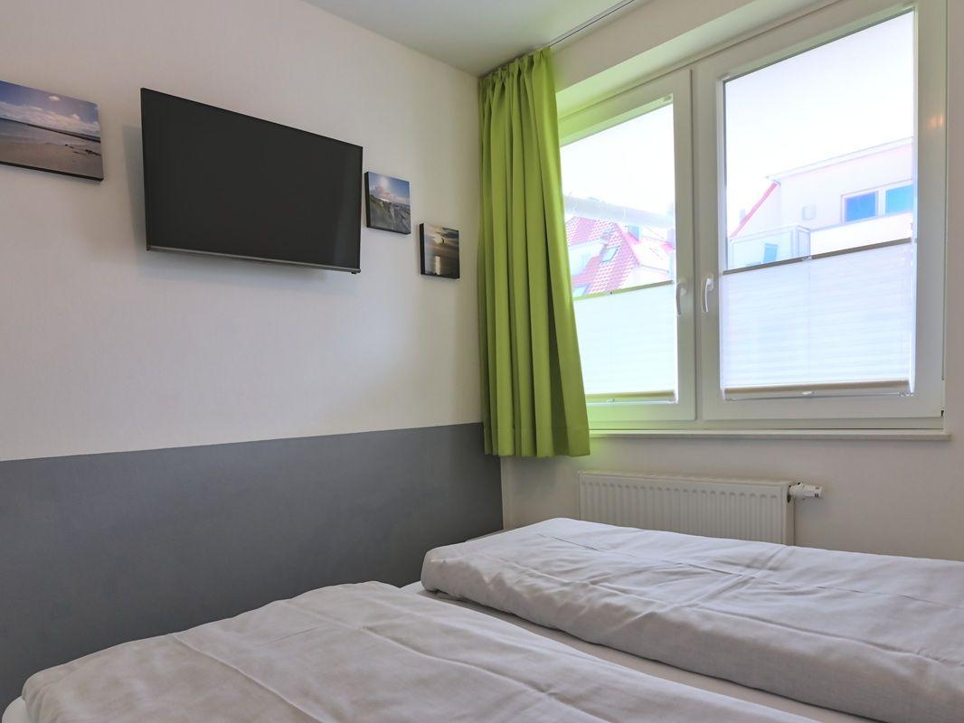 Zimmer mit zwei Betten, Fernseher und Fenster mit grünen Vorhängen.