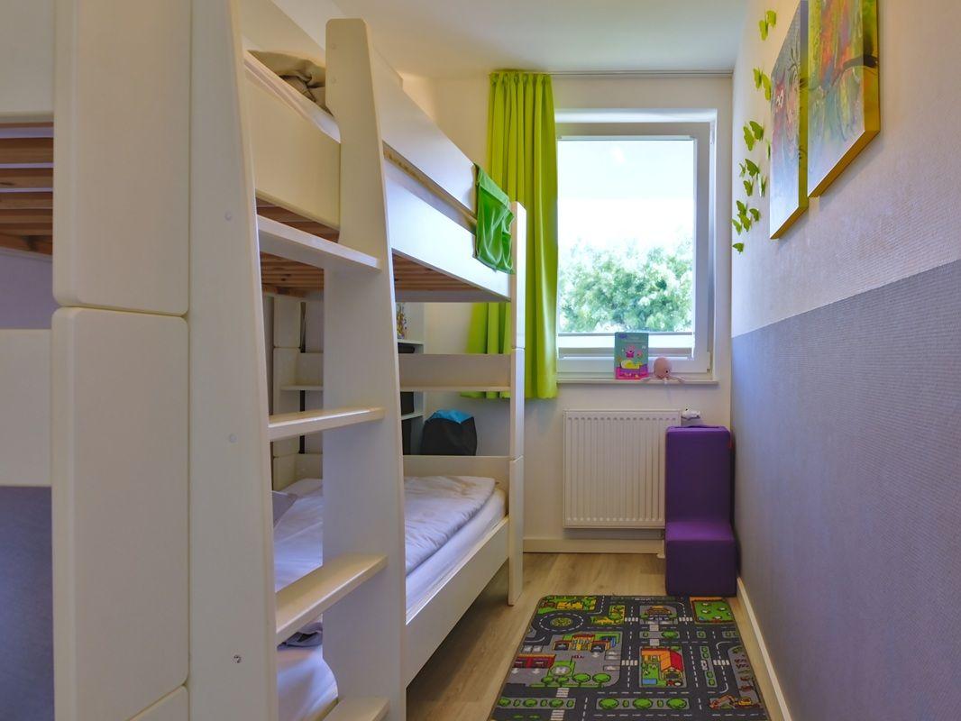 Zimmer mit Doppelstockbett, Fenster mit grünen Vorhängen und Kinderbildern an der Wand.