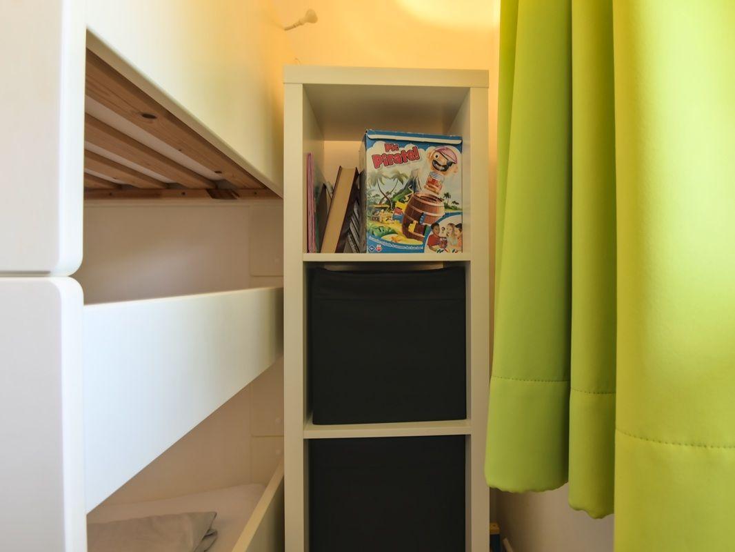 Bett mit Regal und Spielzeugkiste neben grüner Gardine