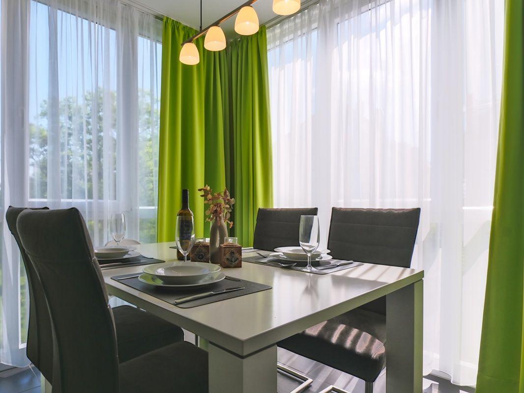 Esstisch mit Stühlen und Fenster mit grünen Vorhängen.