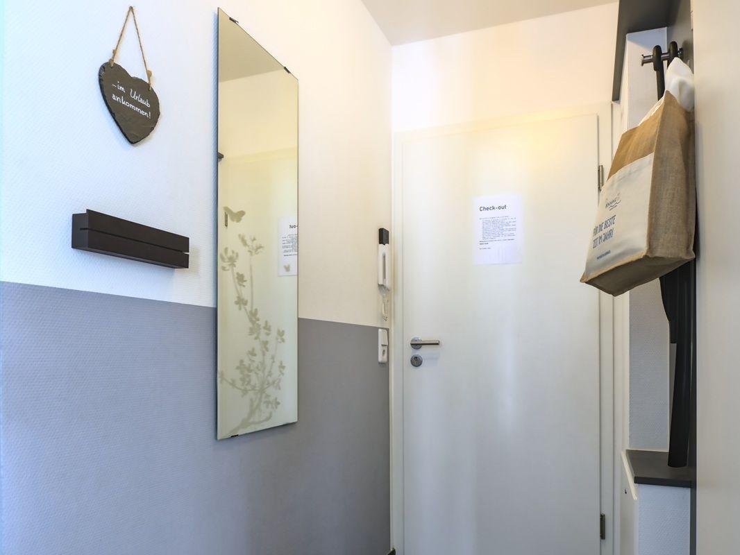 Hausgang mit Spiegel, Herz-Schild und Check-out-Bogen an der Tür.