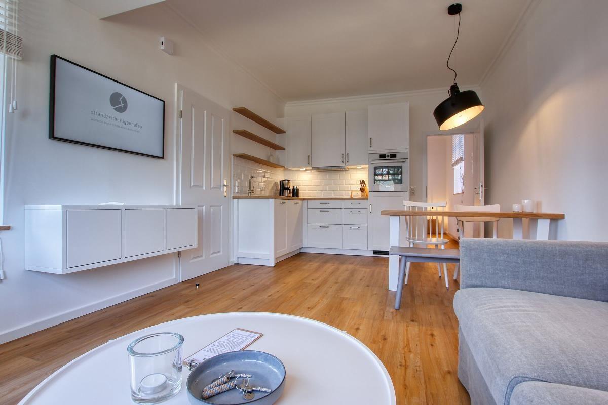 Wohnbereich mit Küche, Esstisch und Sofa. Flur mit Wand-TV und Holzboden.