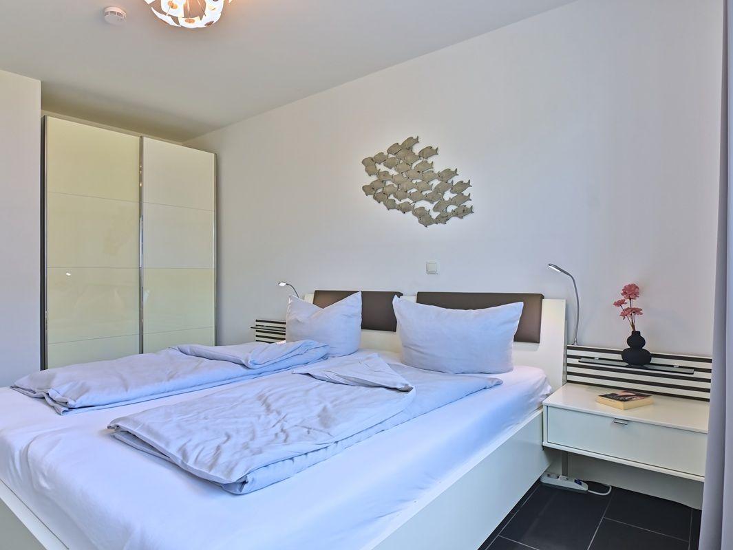 Schlafzimmer mit Doppelbett, Nachttisch und Kleiderschrank. Wanddekoration mit Fischmotiv.