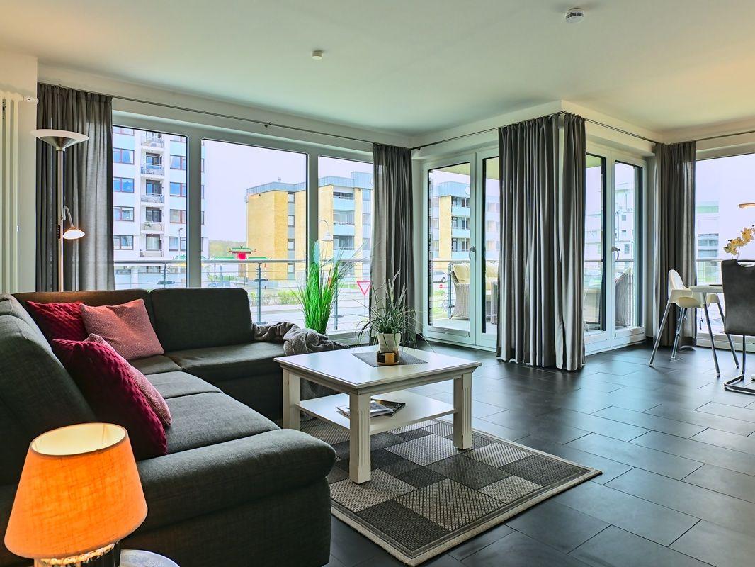 Wohnzimmer mit Sofa, Tisch und großen Fenstern. Blick auf Balkon und Gebäude.