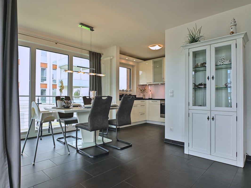 Essbereich mit Tisch, Stühlen und Blick auf Balkon. Weiße Küchenzeile und Schrank im Hintergrund.