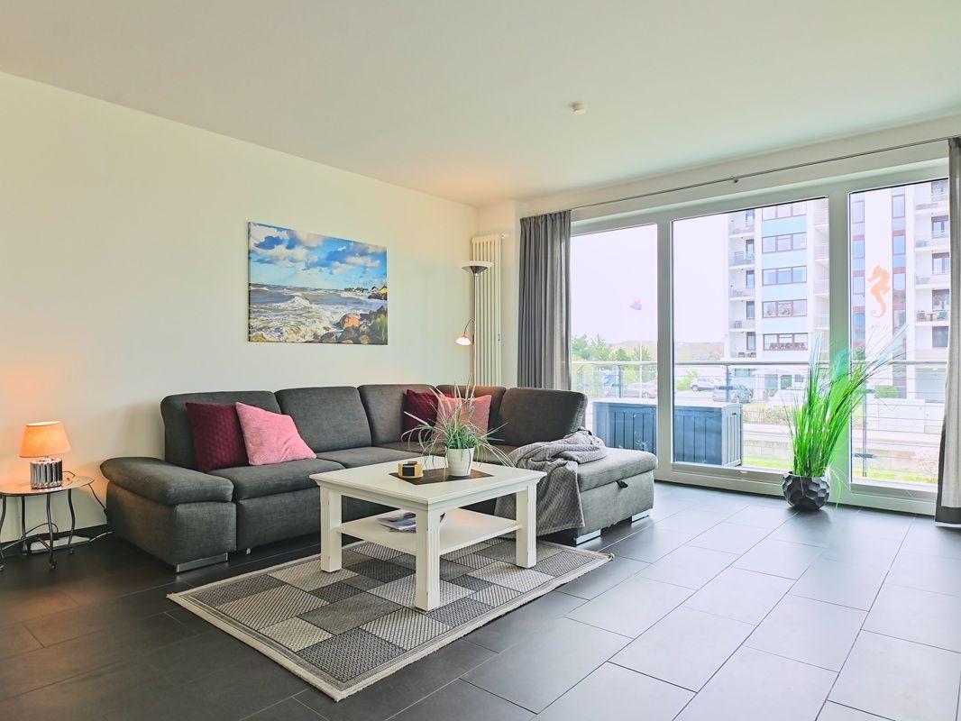 Wohnzimmer mit grauem Sofa, weißem Tisch und Blick auf Balkon.