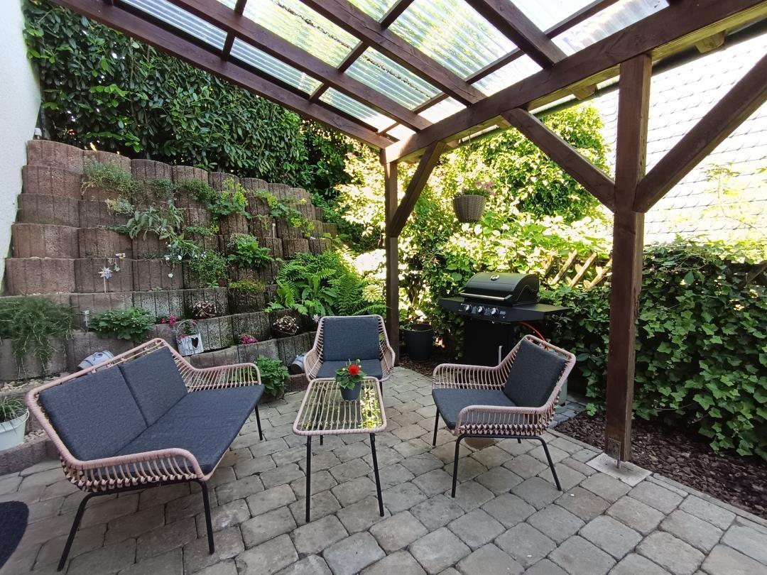 Garden area with seating, grill, and plants under glass roof.
