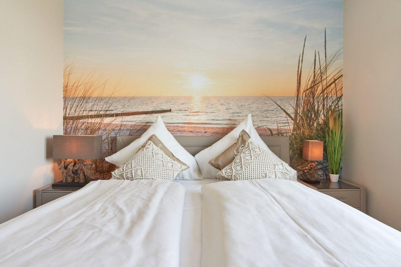 Schlafzimmer mit Bett, Kissen und Wandbild von Strand und Sonnenuntergang.
