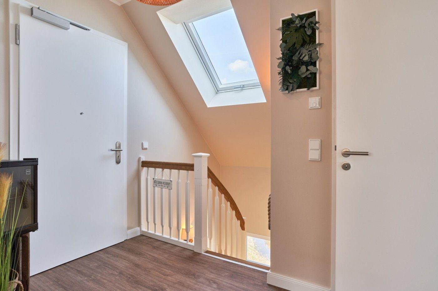 Eingangsbereich mit Treppe, Dachfenster und Tür. Wandbild und Holzboden sichtbar.