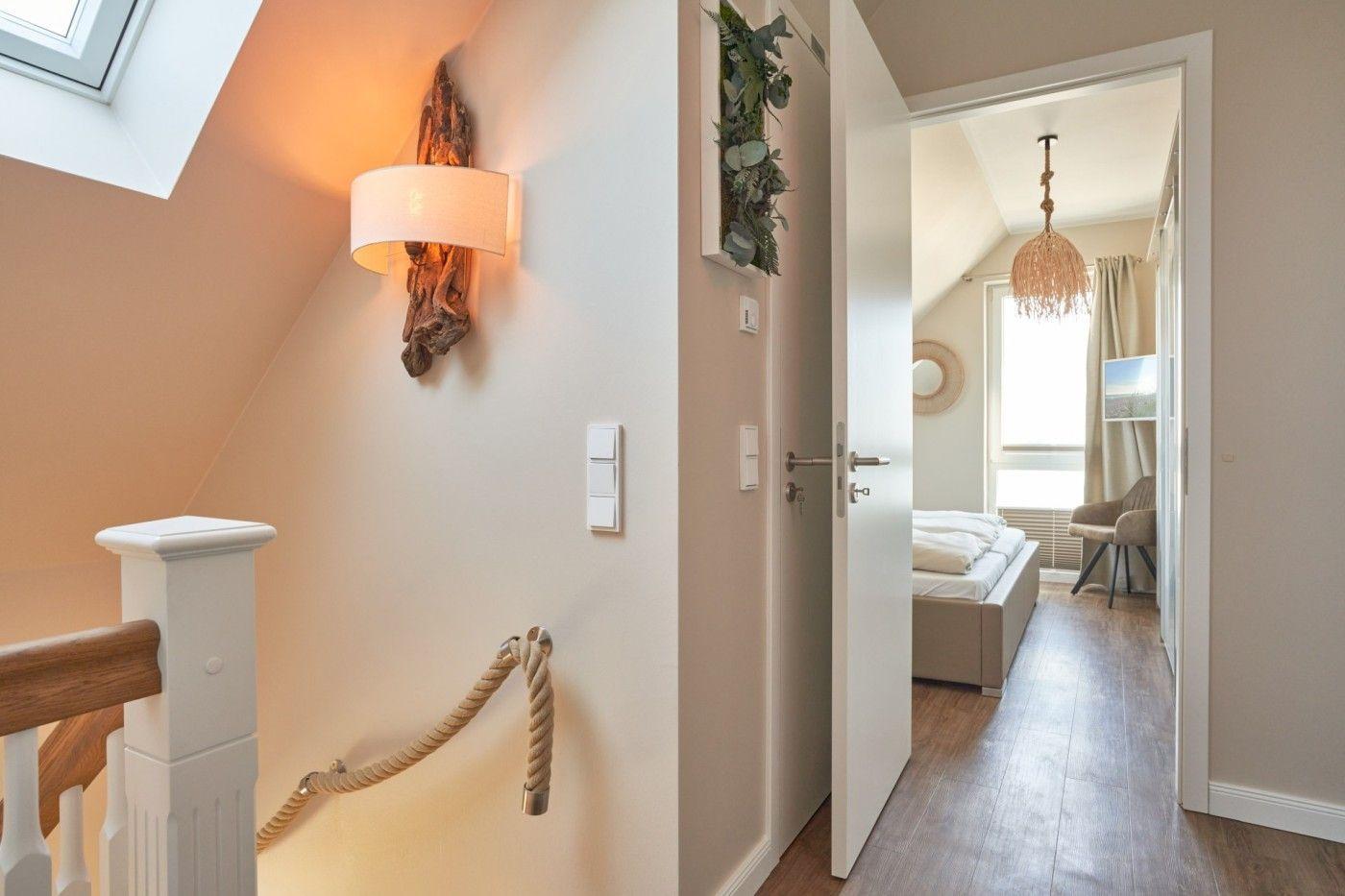 Haus mit Schlafzimmer und Dachschrägen. Holzgeländer und Wandlampe sichtbar.