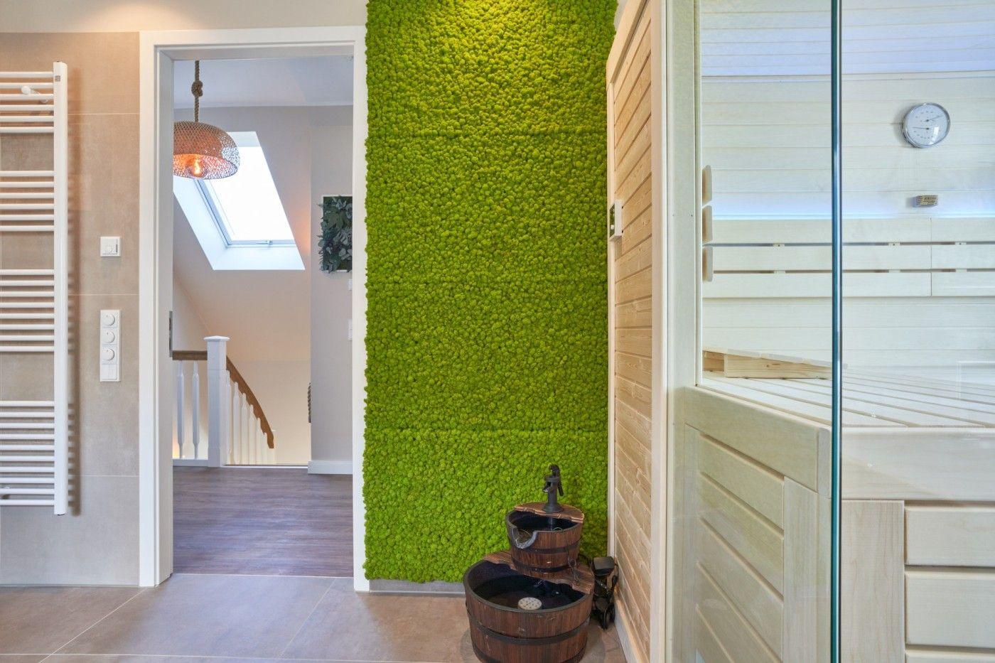 Sauna mit Glaswand, grüner Wandteppich und Holzregal im Hintergrund.