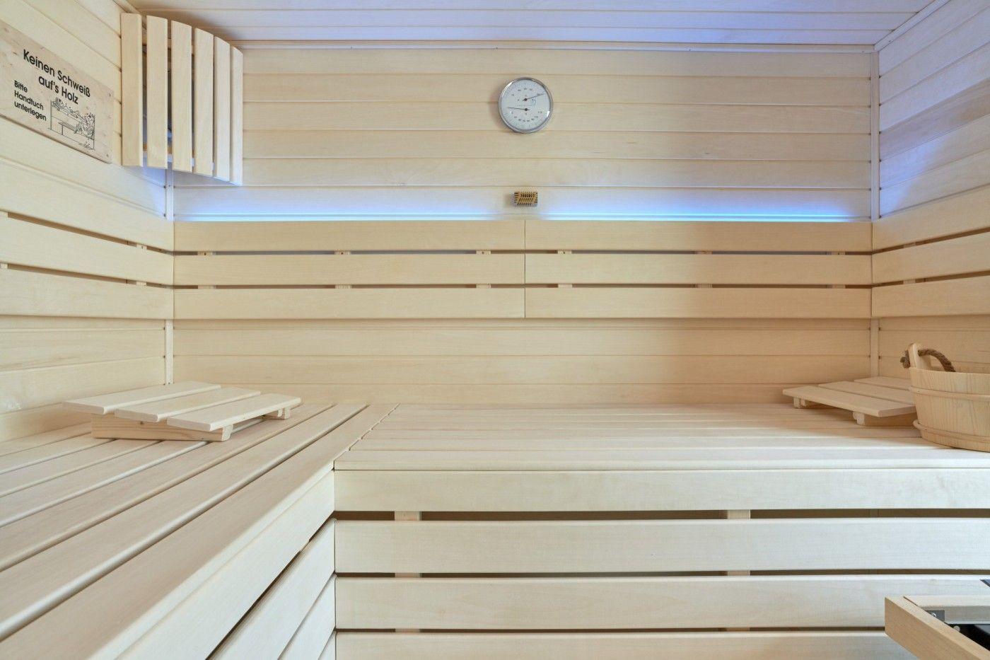 Holzsauna mit Sitzbänken, Thermometer und Eimer.