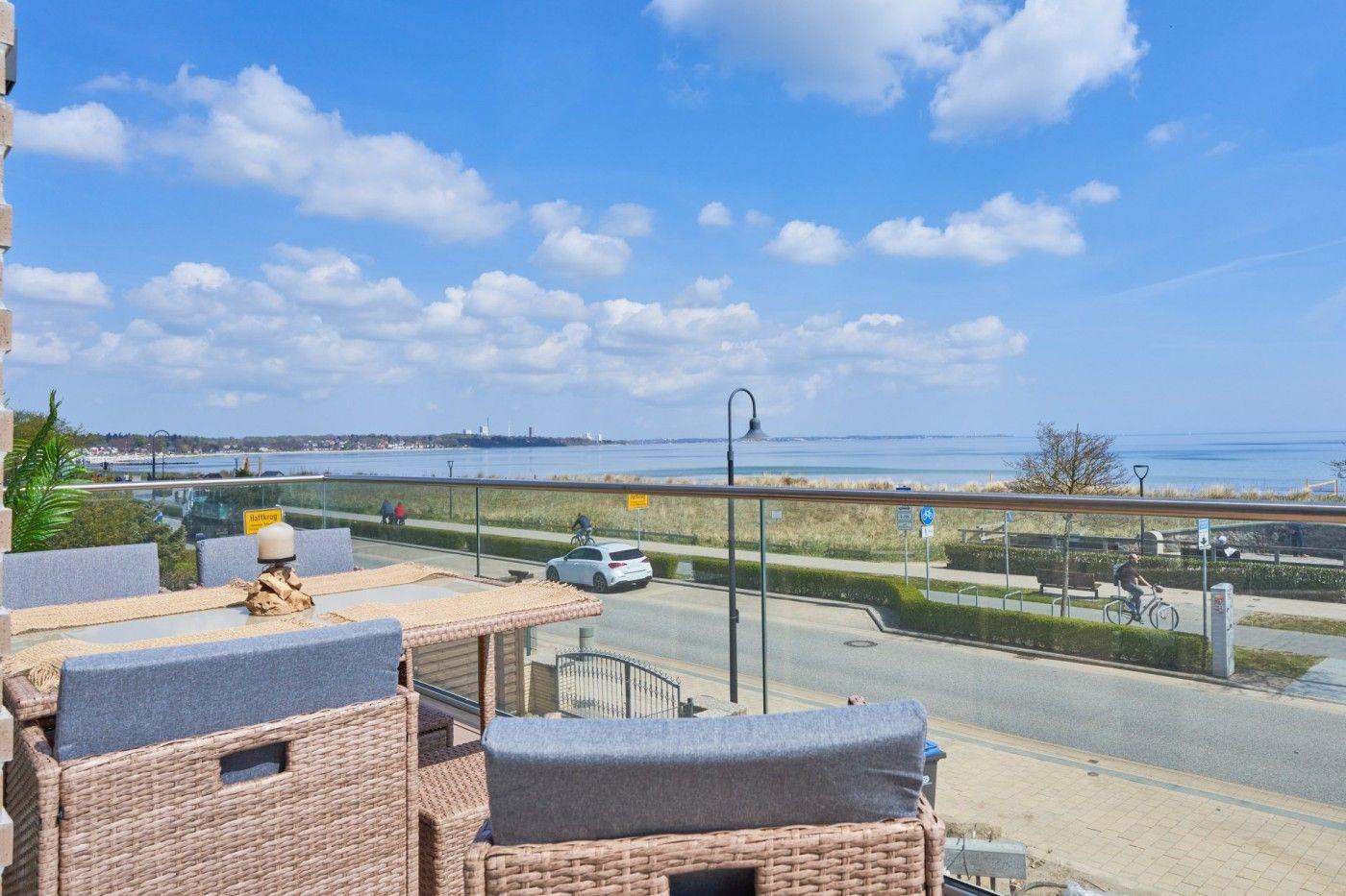 Terrasse mit Sitzgelegenheiten und Blick auf Wasser und Strandpromenade.