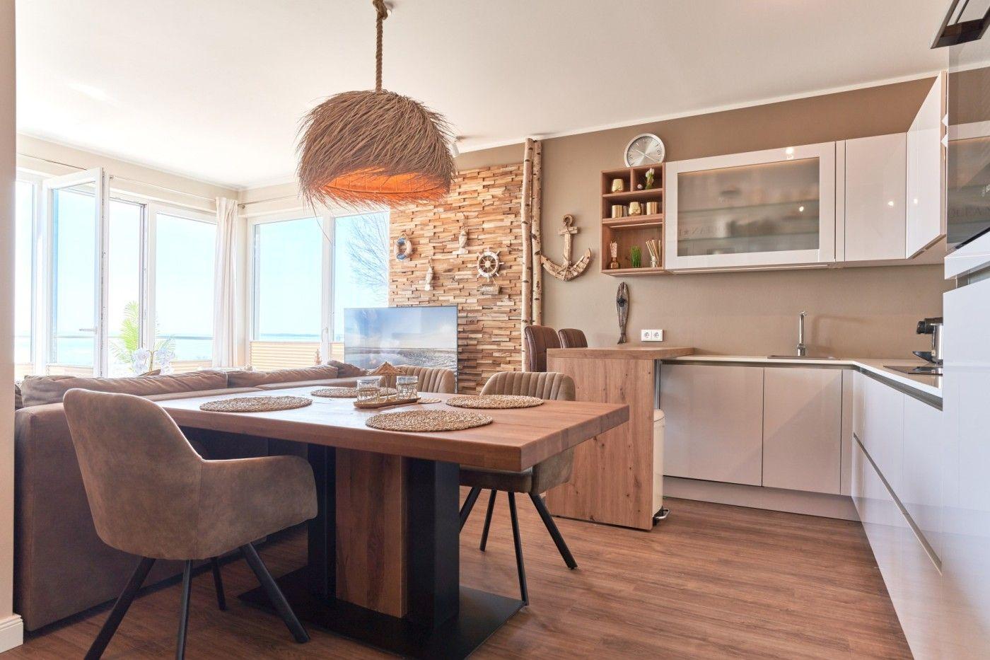 Essbereich mit Holztisch, Stühlen und Küchenzeile. Große Fenster mit Meerblick.