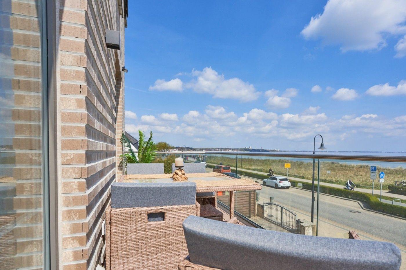 Terrasse mit Sitzgelegenheiten und Blick auf Straße und Wasser.