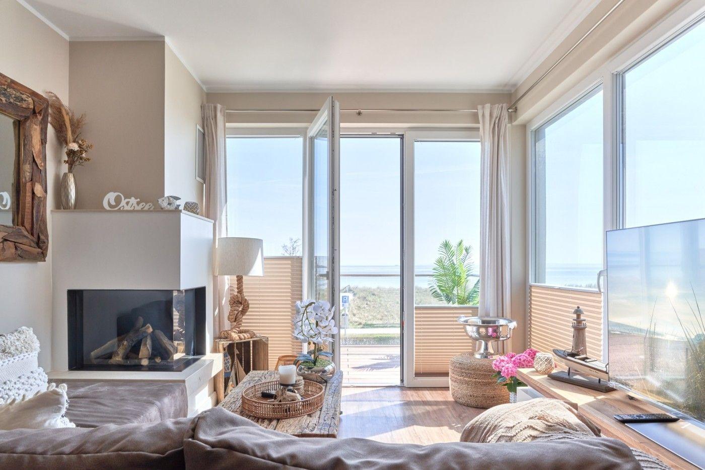 Wohnzimmer mit Kamin, Fernseher und Meerblick durch große Fenster.