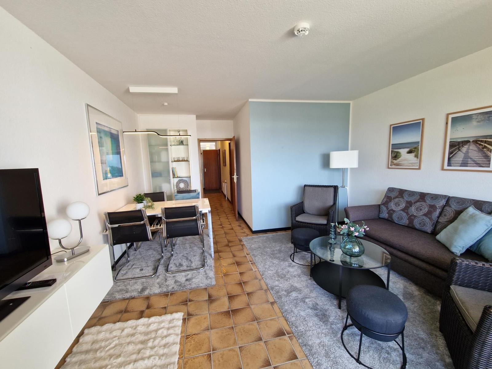 Wohn- und Essbereich mit Sofa, Tisch und Stühlen sowie Fernseher und Bildern an den Wänden.