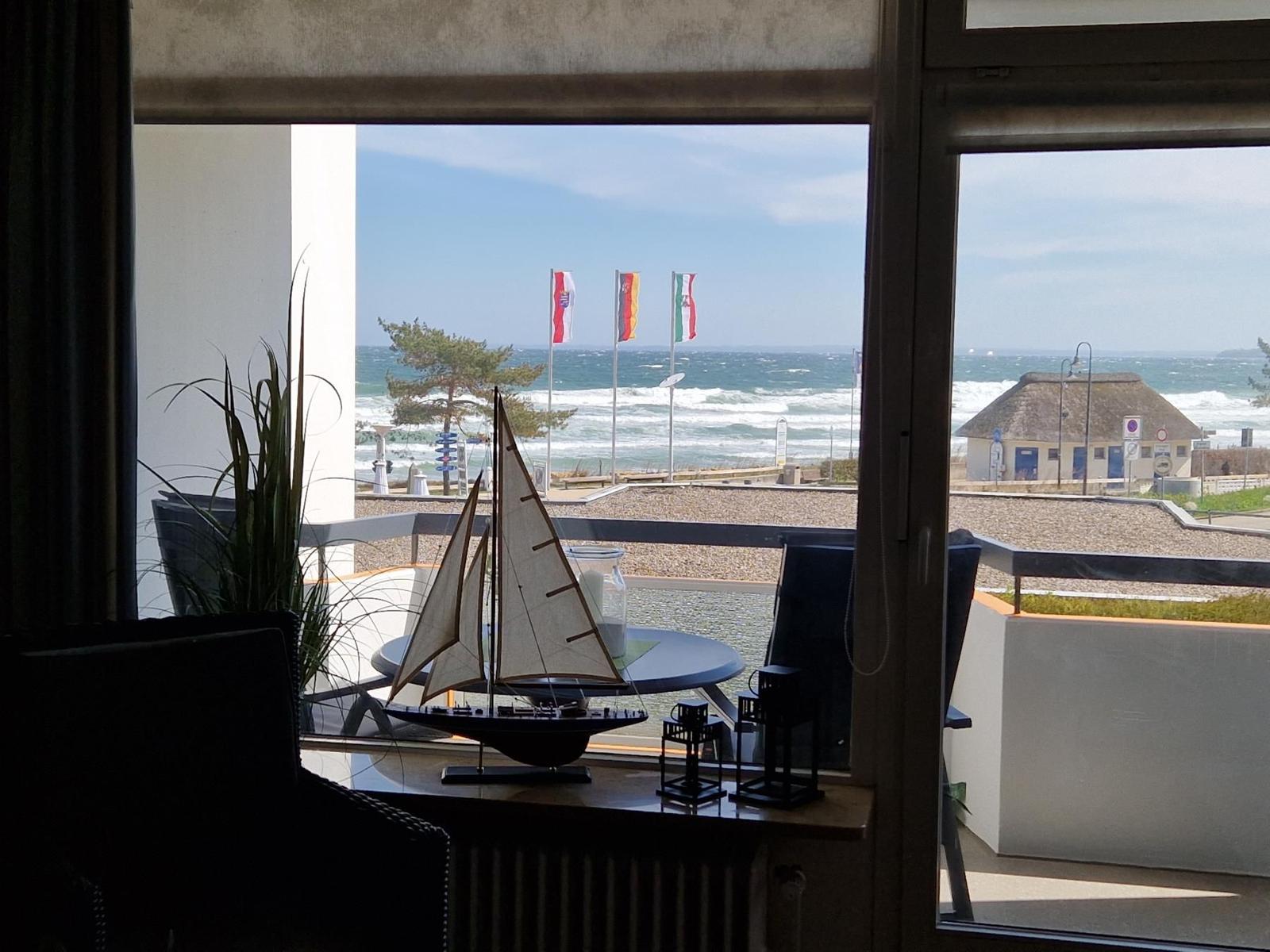 Blick vom Balkon auf das Meer mit Wellen und Flaggen. Modellboot auf Tisch.