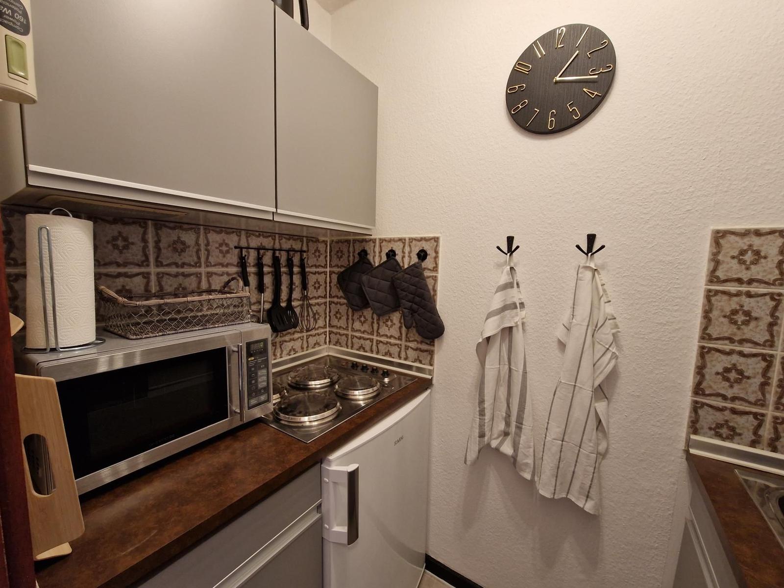 Küche mit Mikrowelle, Herd, Kühlschrank und Wanduhr.