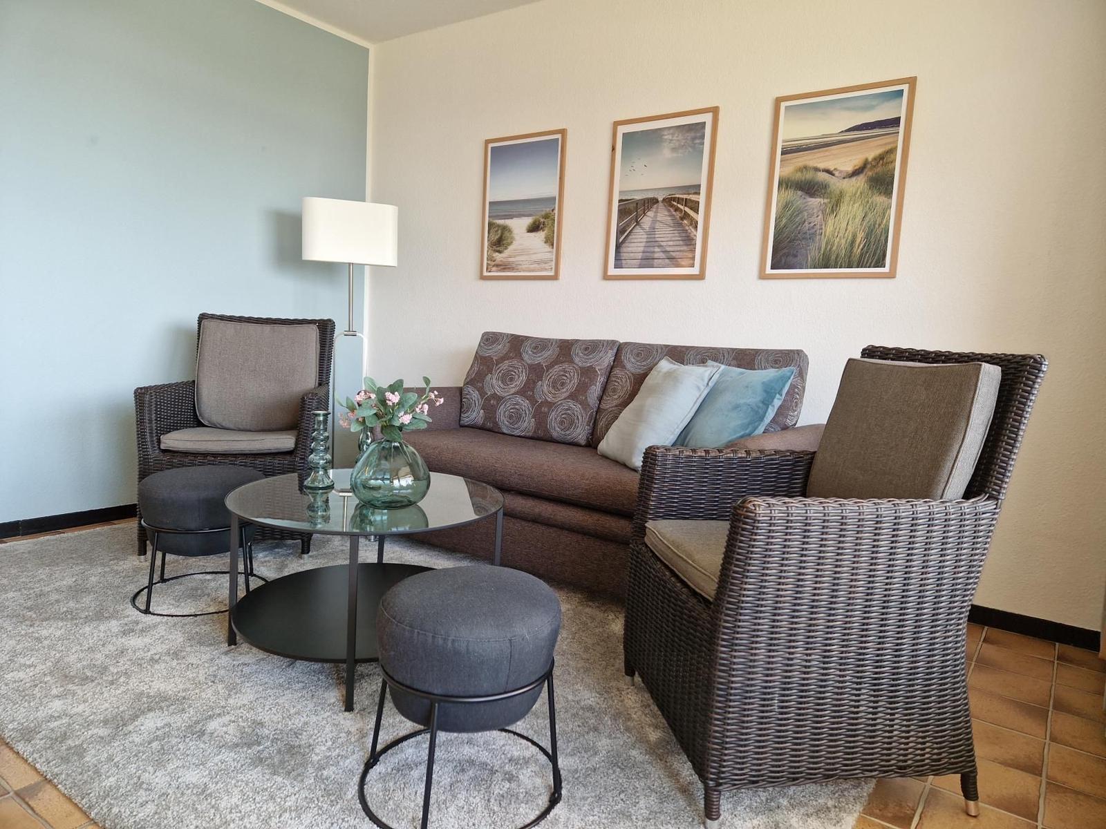 Wohnzimmer mit Sofa, zwei Sesseln und runden Tischen auf Teppich.