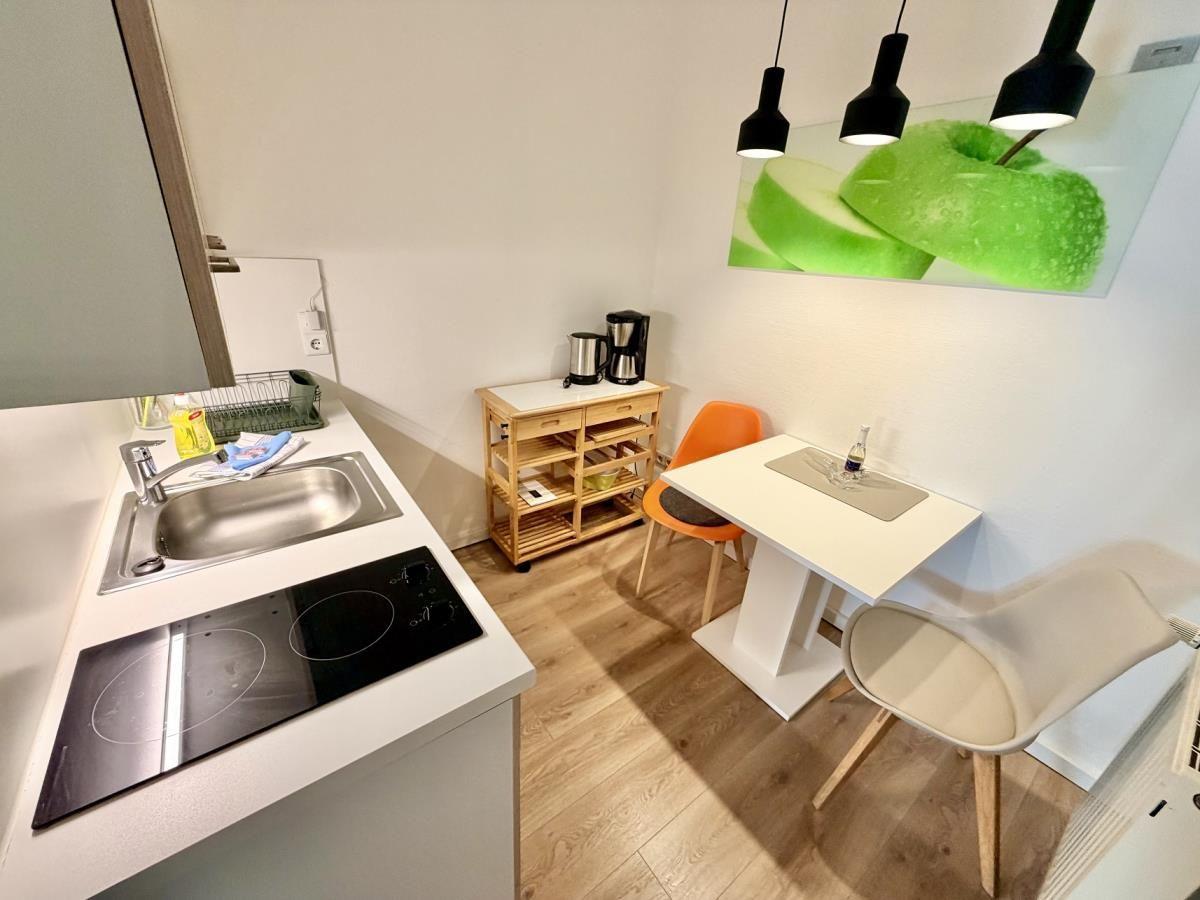 Küche mit Induktionskochfeld, Spüle und Esstisch mit zwei Stühlen.