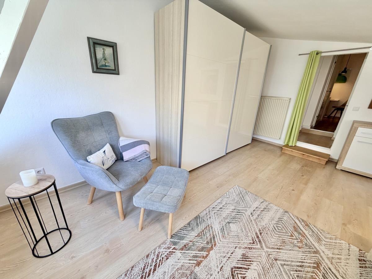 Schlafzimmer mit grauer Sitzgelegenheit, Kleiderschrank und Teppich auf Holzboden