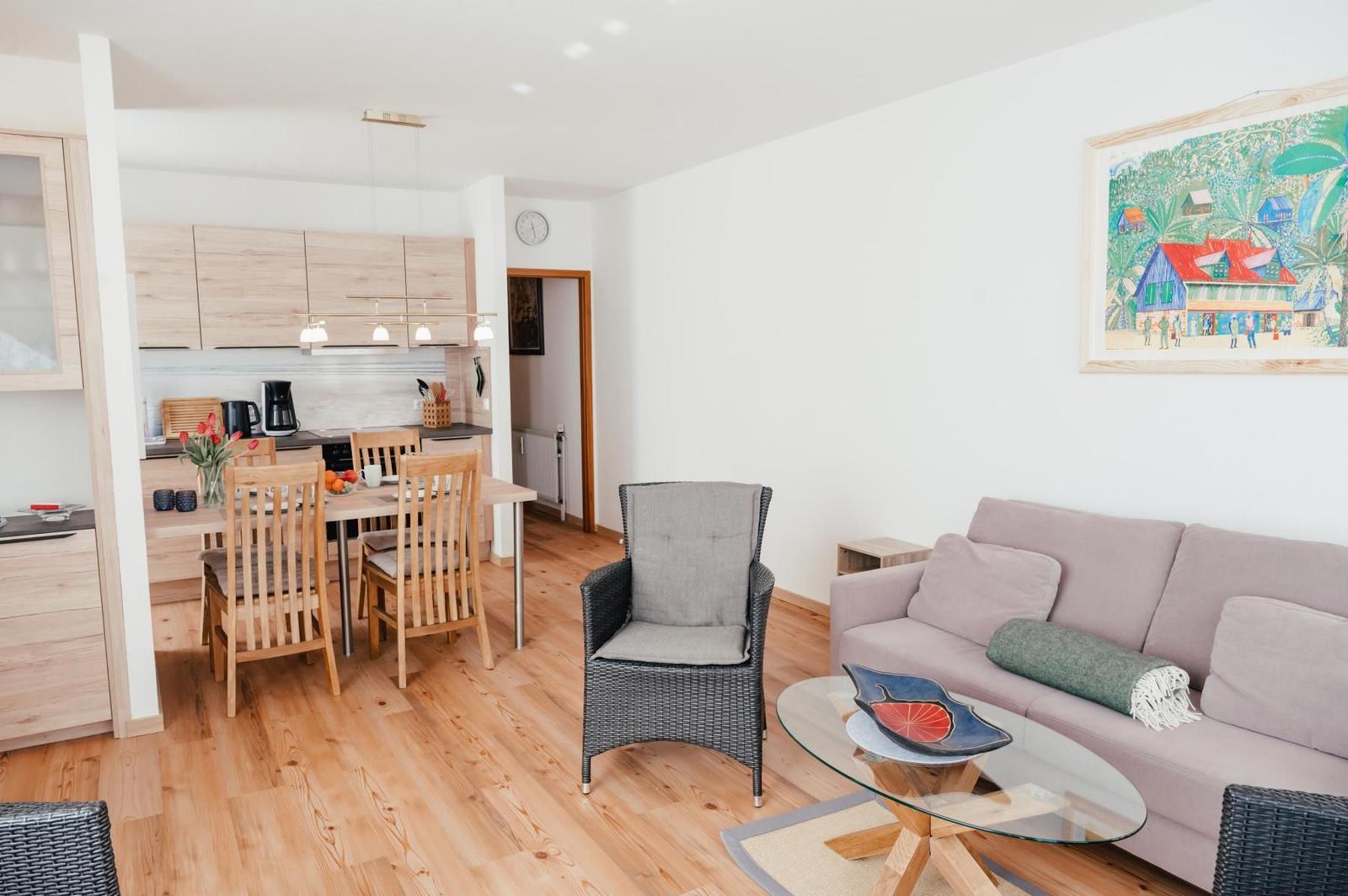 Wohn- und Essbereich mit Küchenzeile, Sofa und Stuhl. Holzboden und Wandbild.