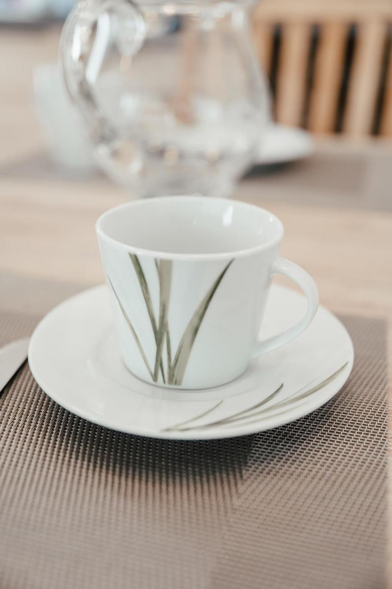 Eine weiße Tasse mit grünem Muster auf Untertasse auf Tisch mit Platzdecke.