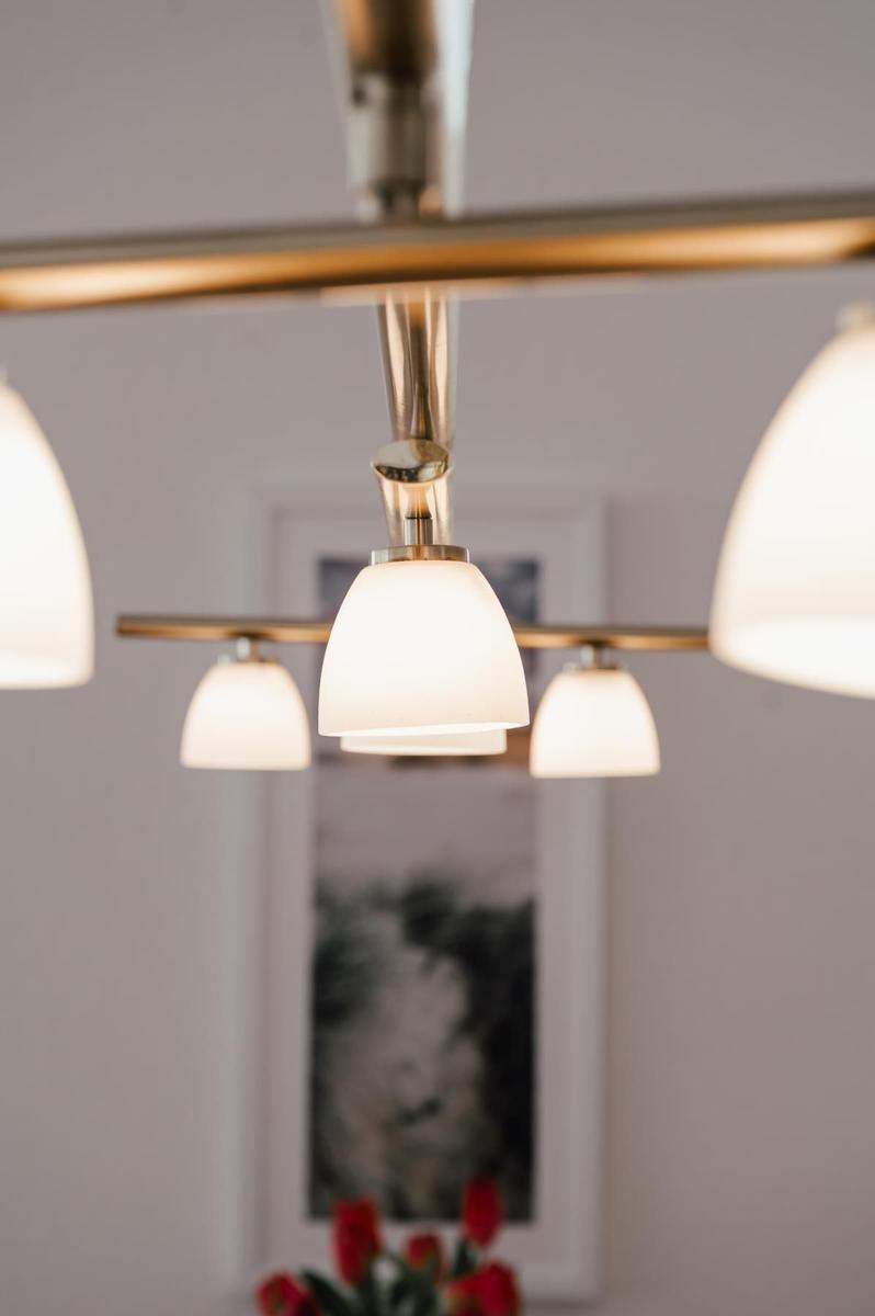 Moderne Deckenleuchte mit weißen Lampenschirmen und goldenen Halterungen hängt in einem Raum mit Wandbild.