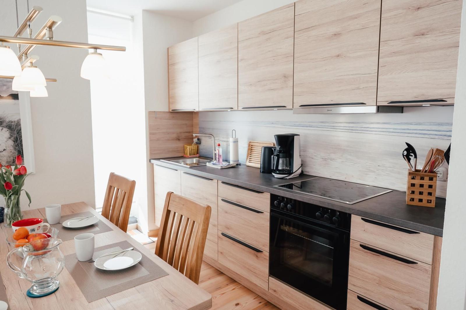 Moderne Küche mit Holzschränken, Kochfeld und Esstisch mit Stühlen.