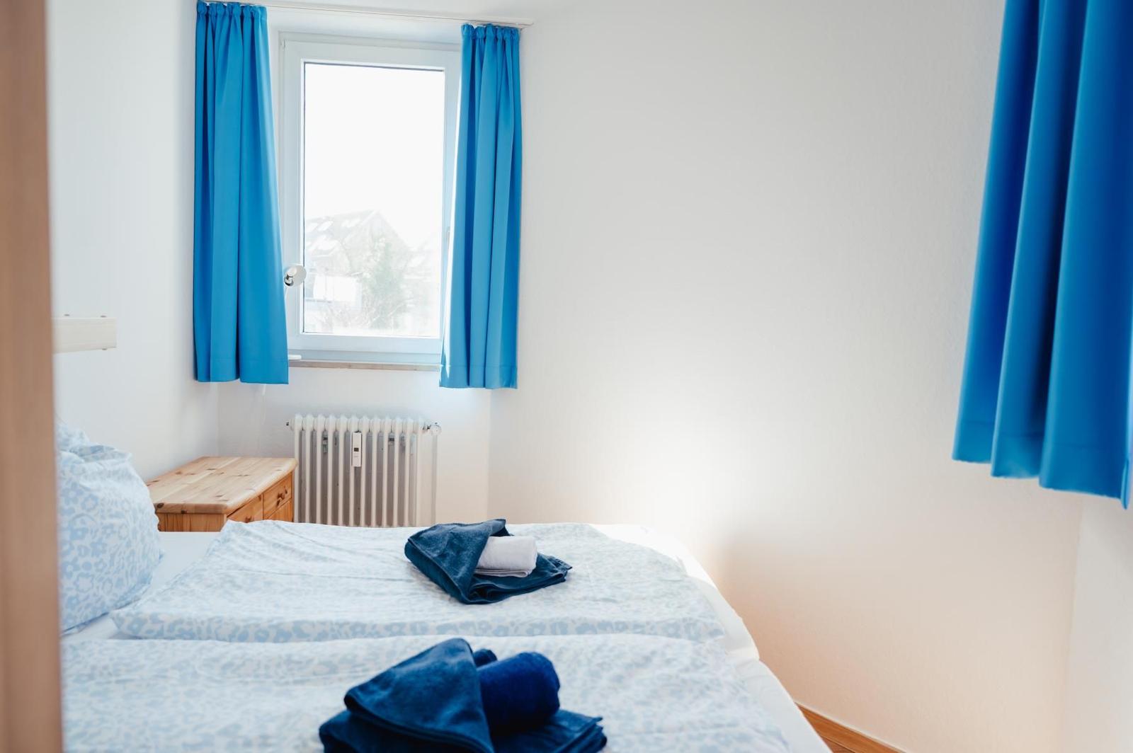 Ein Schlafzimmer mit blauen Vorhängen, einem Fenster und einem Bett mit Bettwäsche.