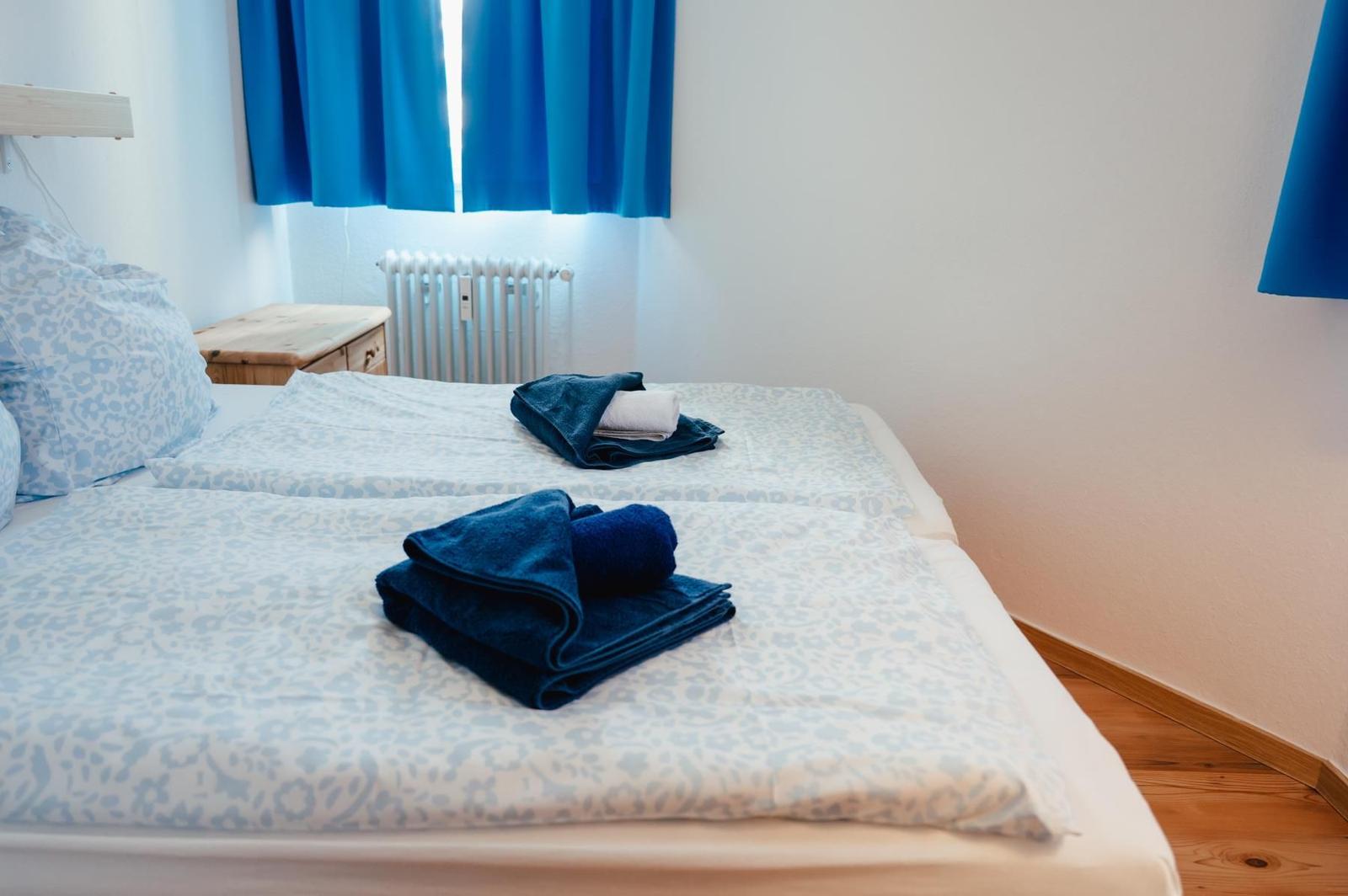 Schlafzimmer mit Bett, blauen Vorhängen und gefalteten Handtüchern.