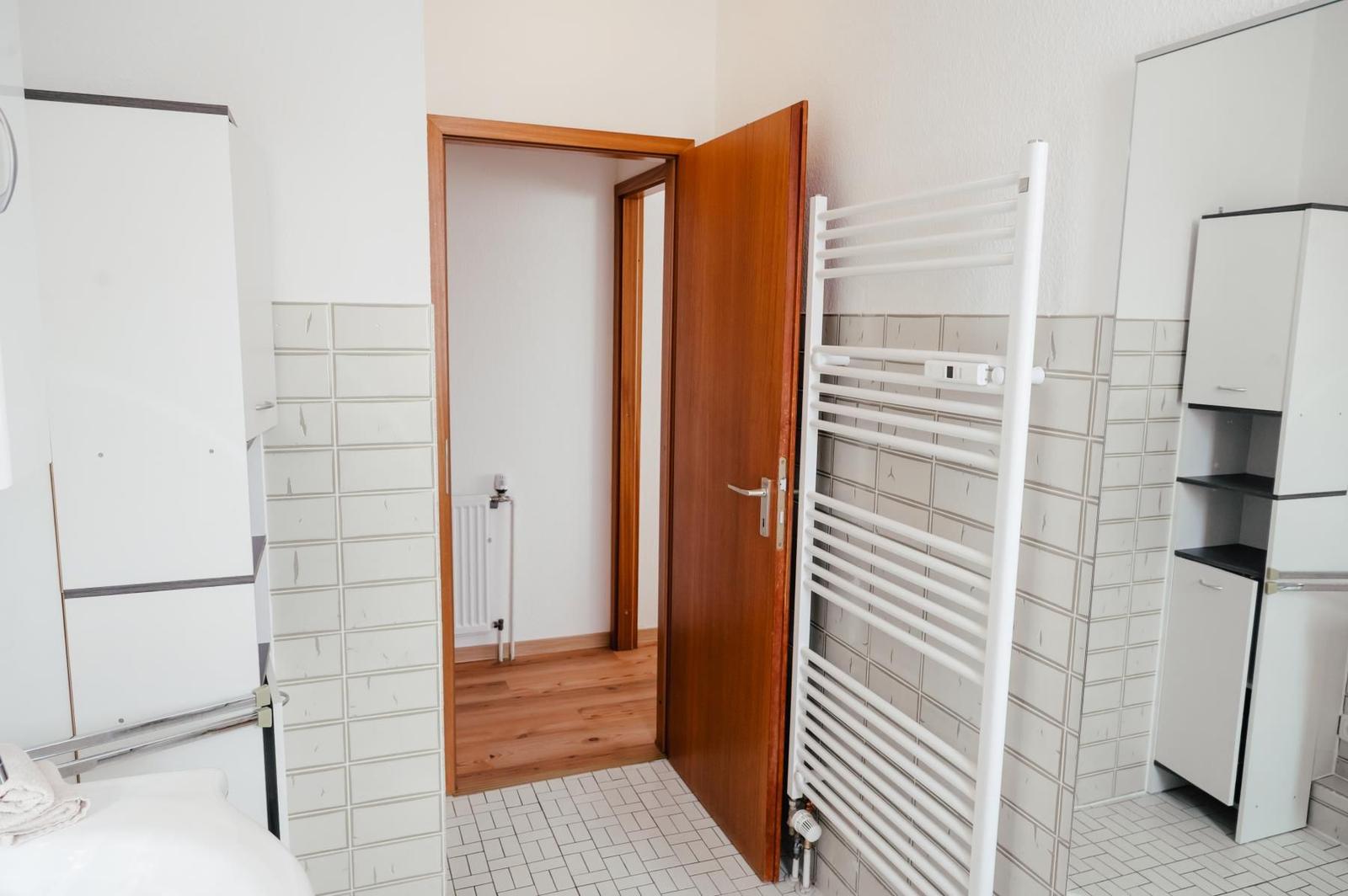 Badezimmer mit Duschbereich, Heizkörper und Holzboden im angrenzenden Raum.