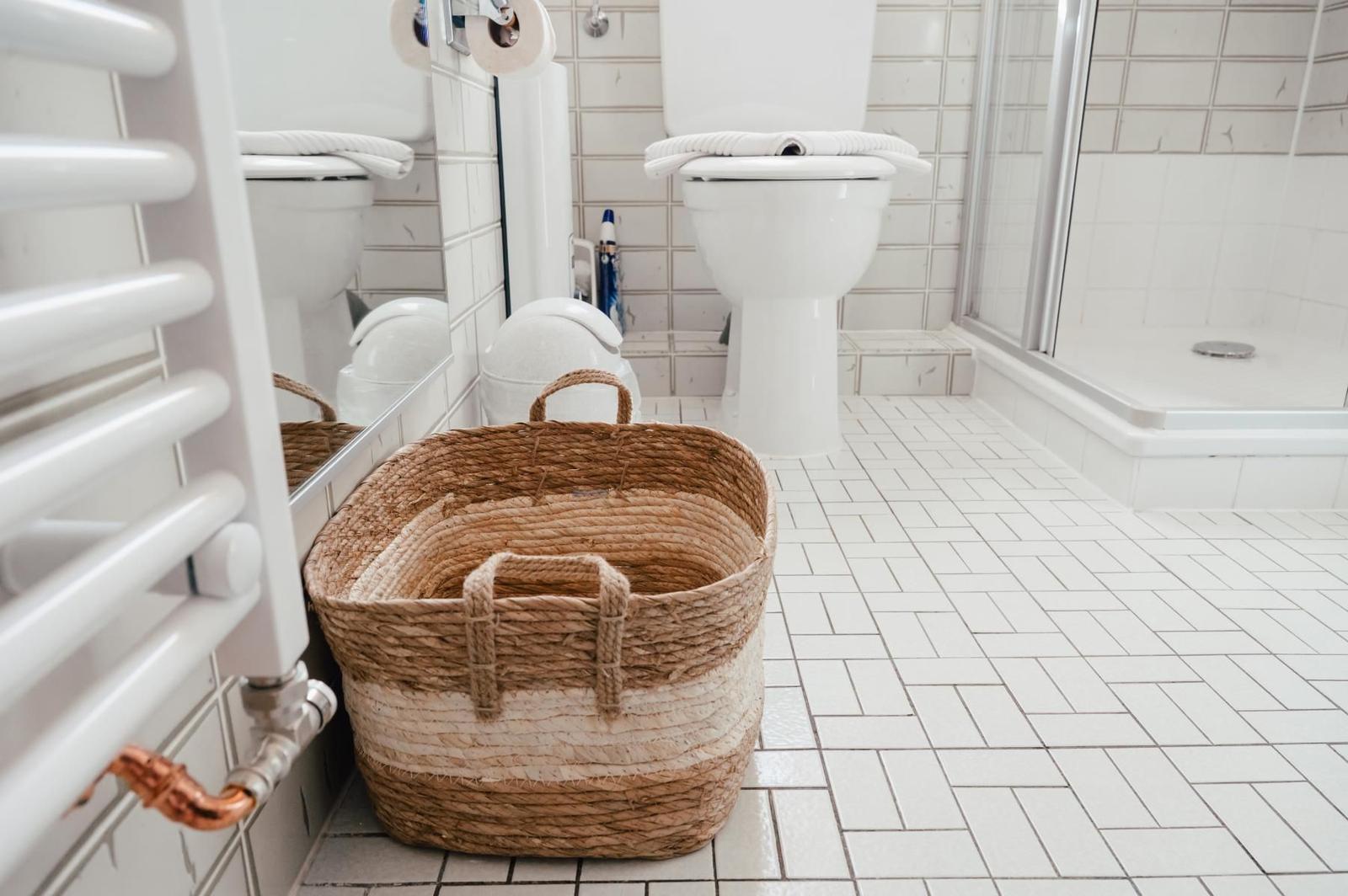 Badezimmer mit Toilette, Dusche und geflochtenem Korb auf Fliesenboden.