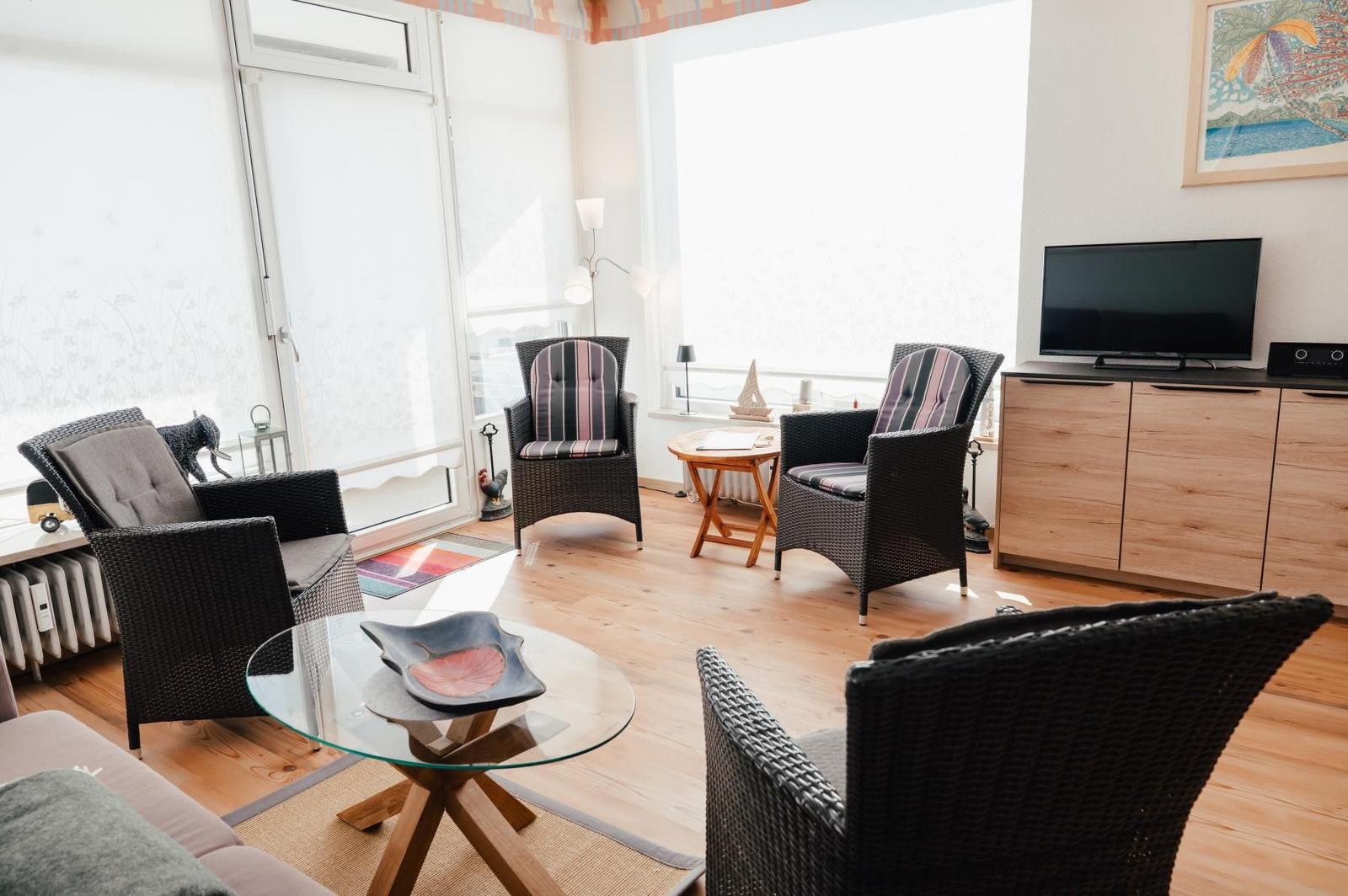 Wohnzimmer mit Wickerstühlen, Glas-Tisch und Fernseher an Wand.