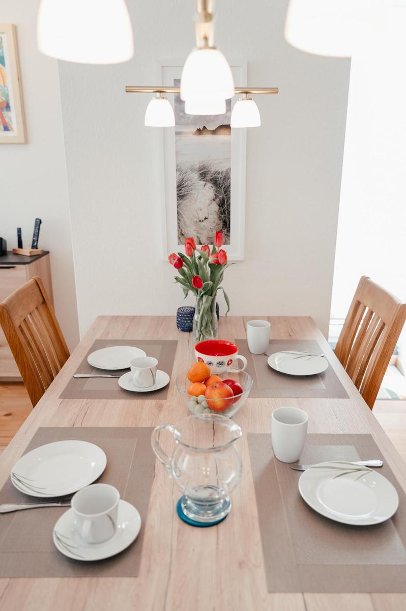 Holztisch mit Platz für vier Personen, Blumen, Obst und Geschirr.