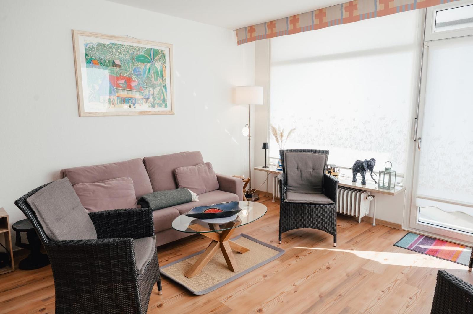 Wohnzimmer mit Sofa, zwei Sesseln, Glas-Tisch und Fenster