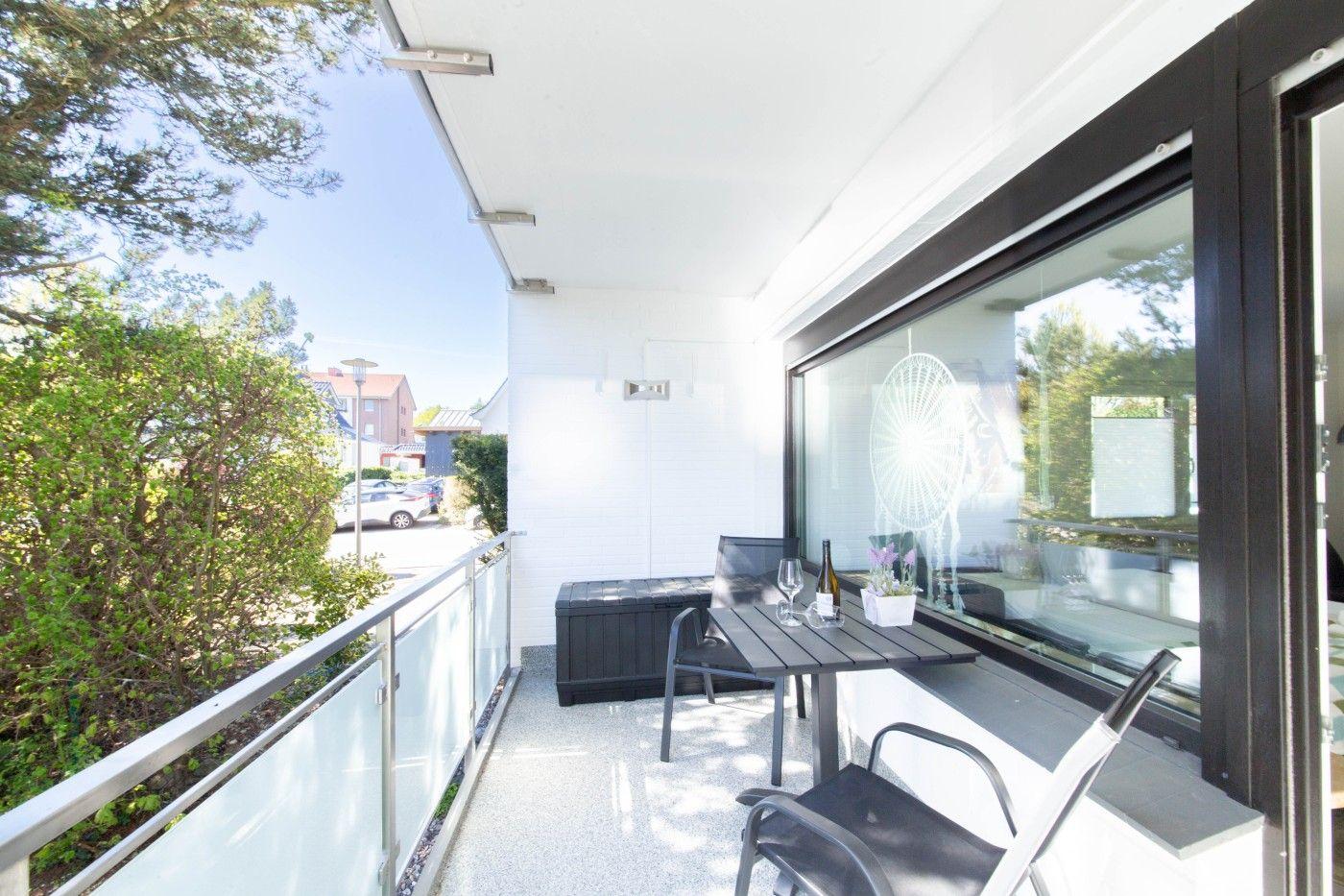 Terrasse mit Tisch, Stühlen und Sitzbank. Glasgeländer und Blick auf Grünflächen.