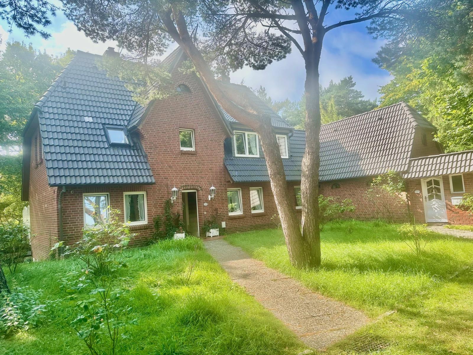 Ein rotes Backsteingebäude mit grauem Dach, umgeben von Gras und Bäumen.