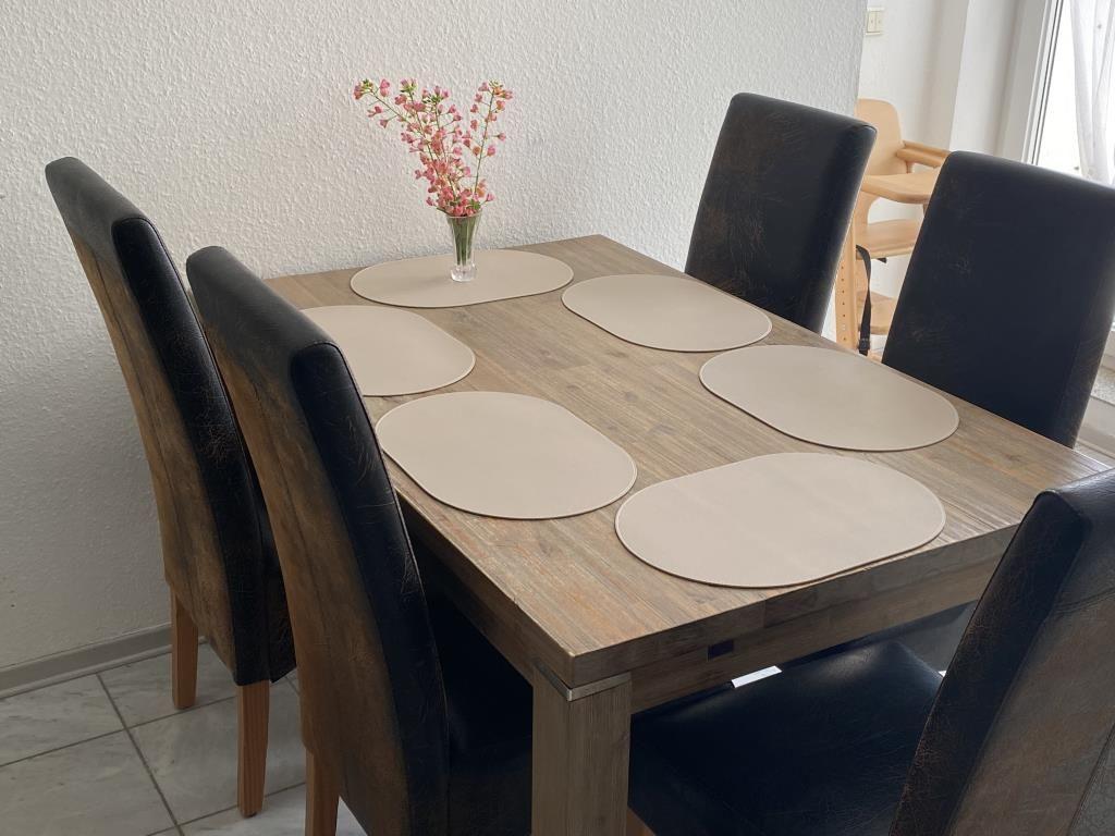 Esszimmer mit Holztisch, sechs Stühlen und Blumenvase.