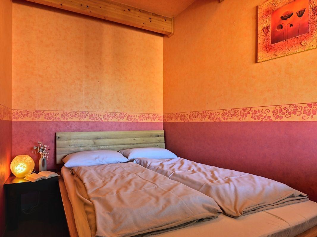 Schlafzimmer mit Doppelbett, Holzkopfteil, Wandgestaltung und Nachttisch mit Lampe.