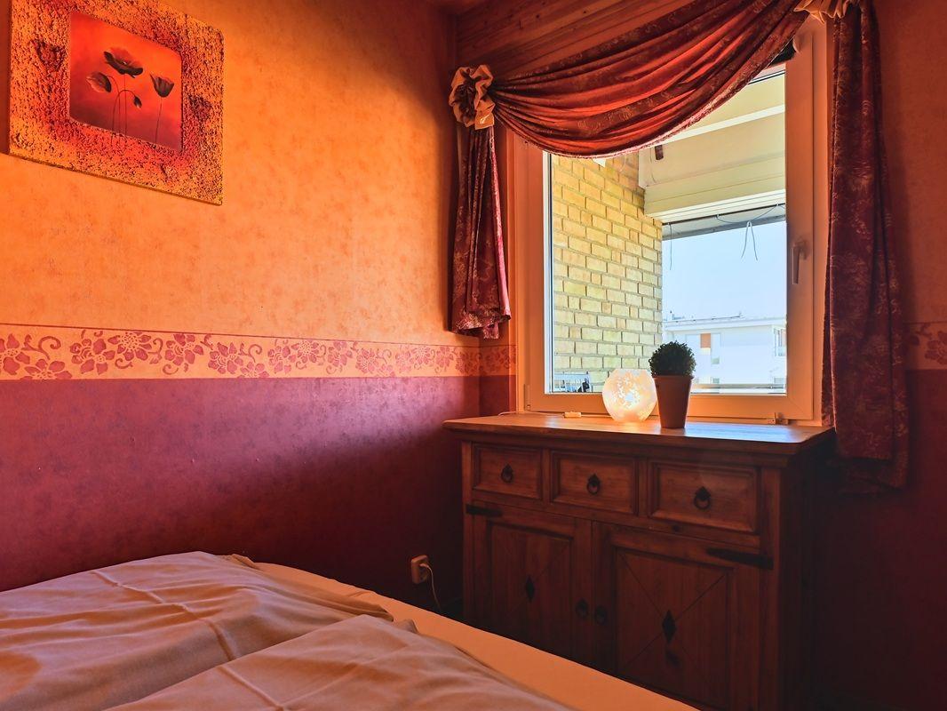 Schlafzimmer mit Bett, Holzschrank und Fenster mit Vorhängen.
