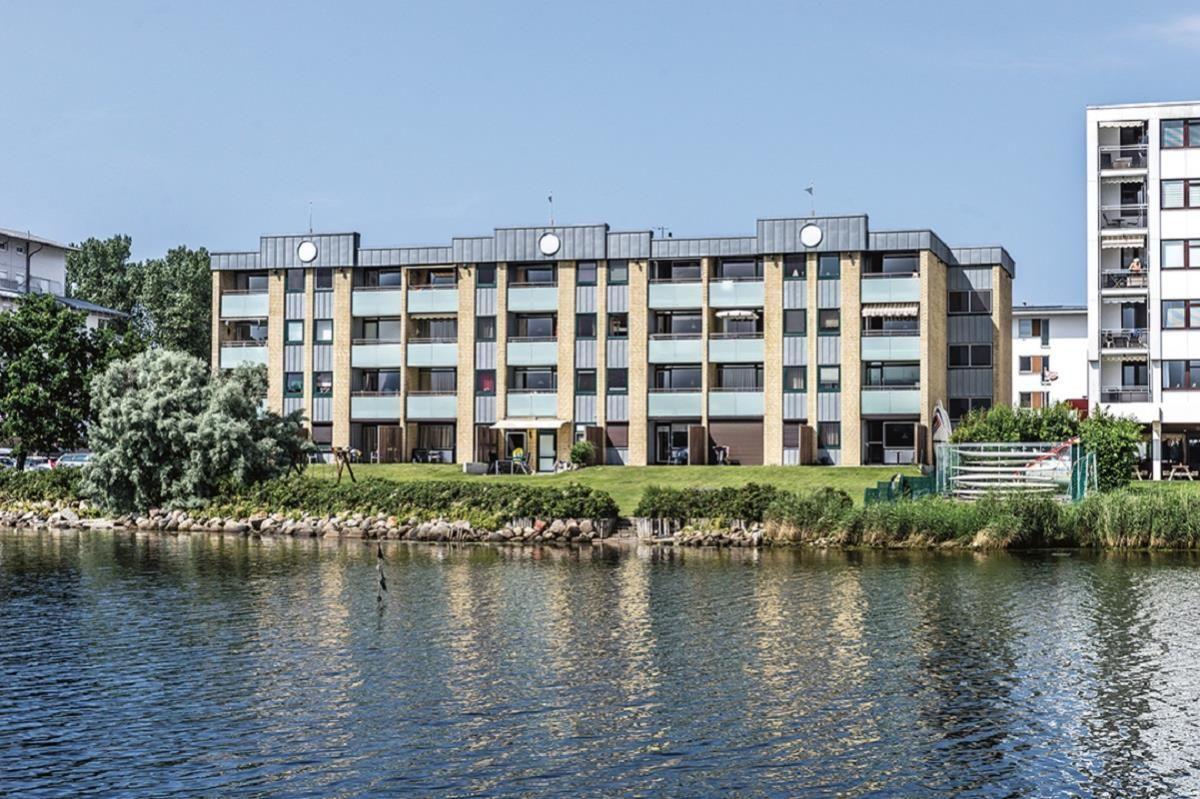 Wohnhaus am Wasser mit Balkonen und grüner Umgebung.